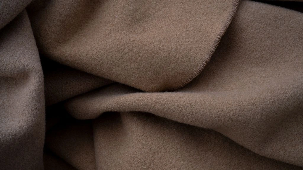 Folded cashmere sweater, leather tote, and sneakers on linen textile